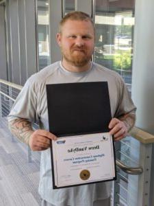 man smiling at camera and holding award certificate